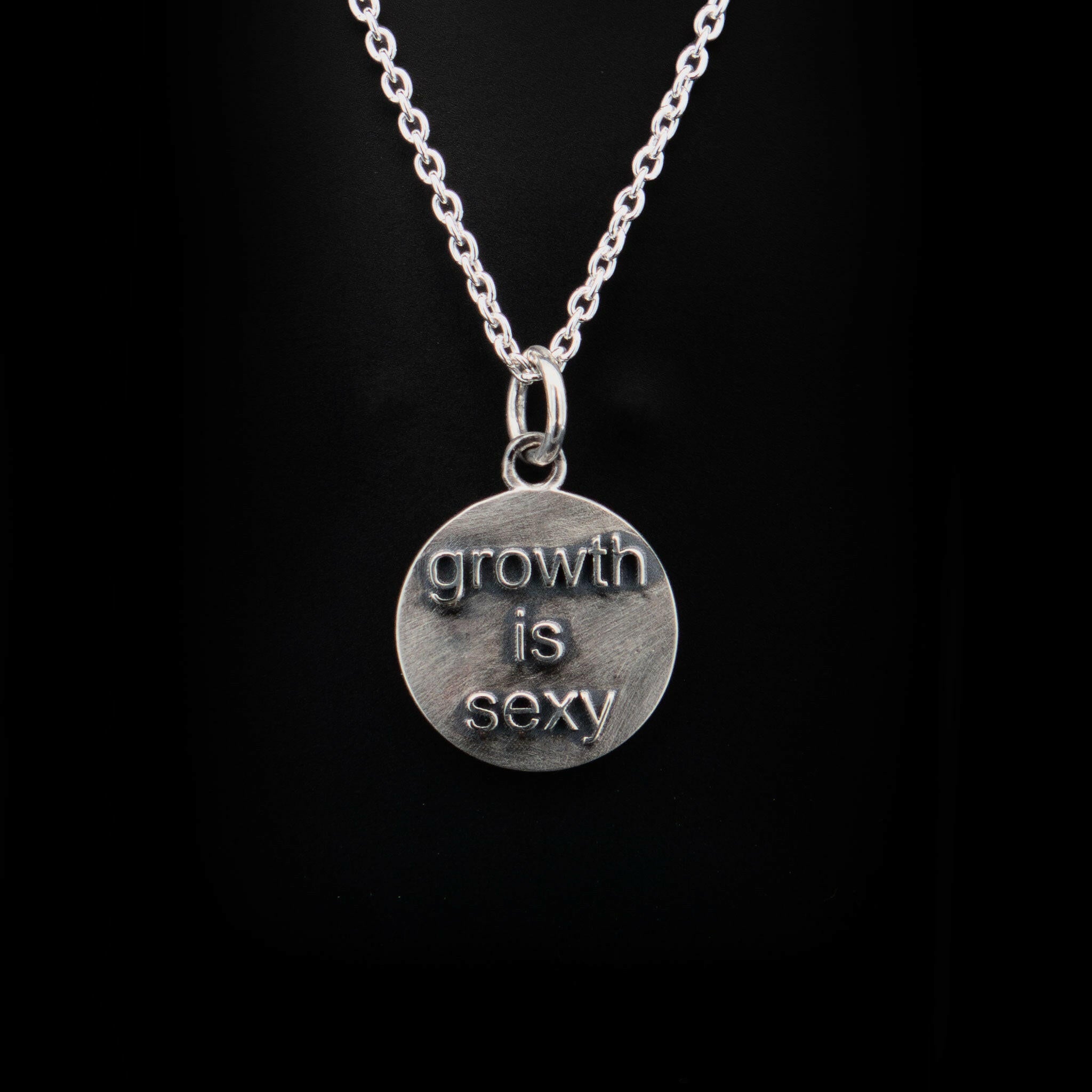 back center of sterling silver round pendant. text reads "growth is sexy" attached to a sterling silver chain and  bail.