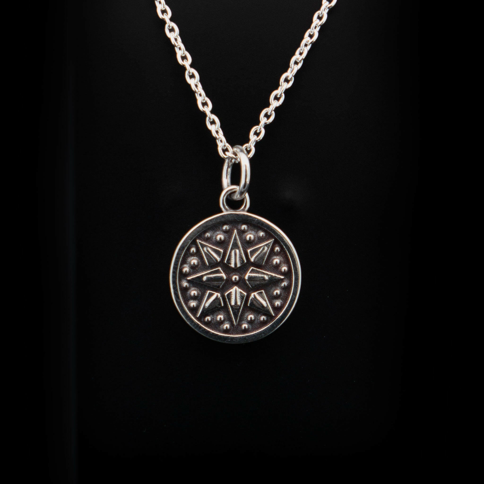 a round silver charm with a silver bail decorated with an  8 pointed star surrounded by circular beads, on a sterling silver cable chain