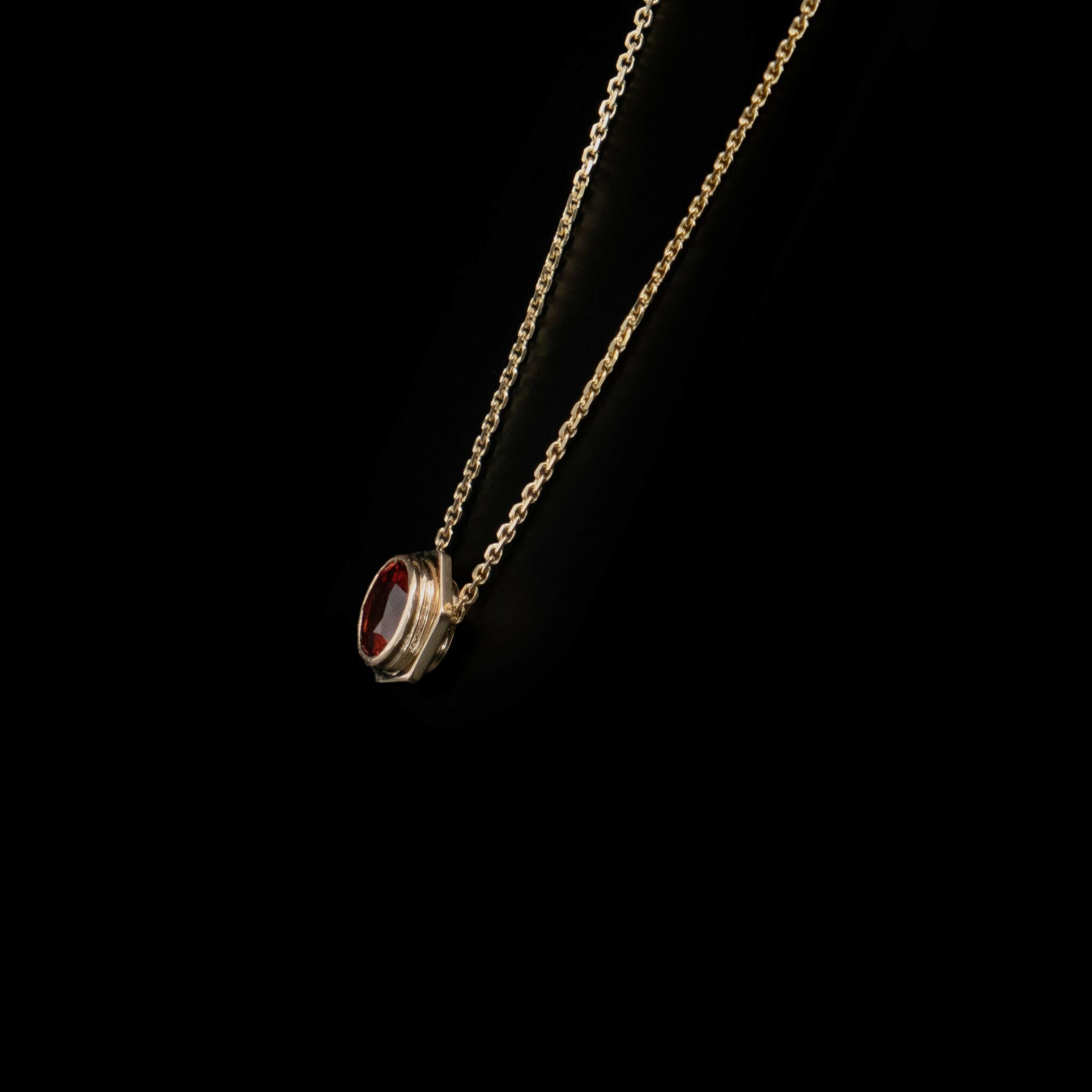 side view of gold yellow bolt pendant with garnet stone centered