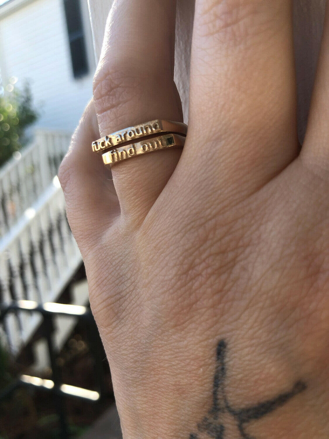 back of hand placed on a wall, two 5 karat yellow gold rings on the ring finger. first (top) ring has texts that reads "fuck around", second (bottom) ring has text that reads "find out"