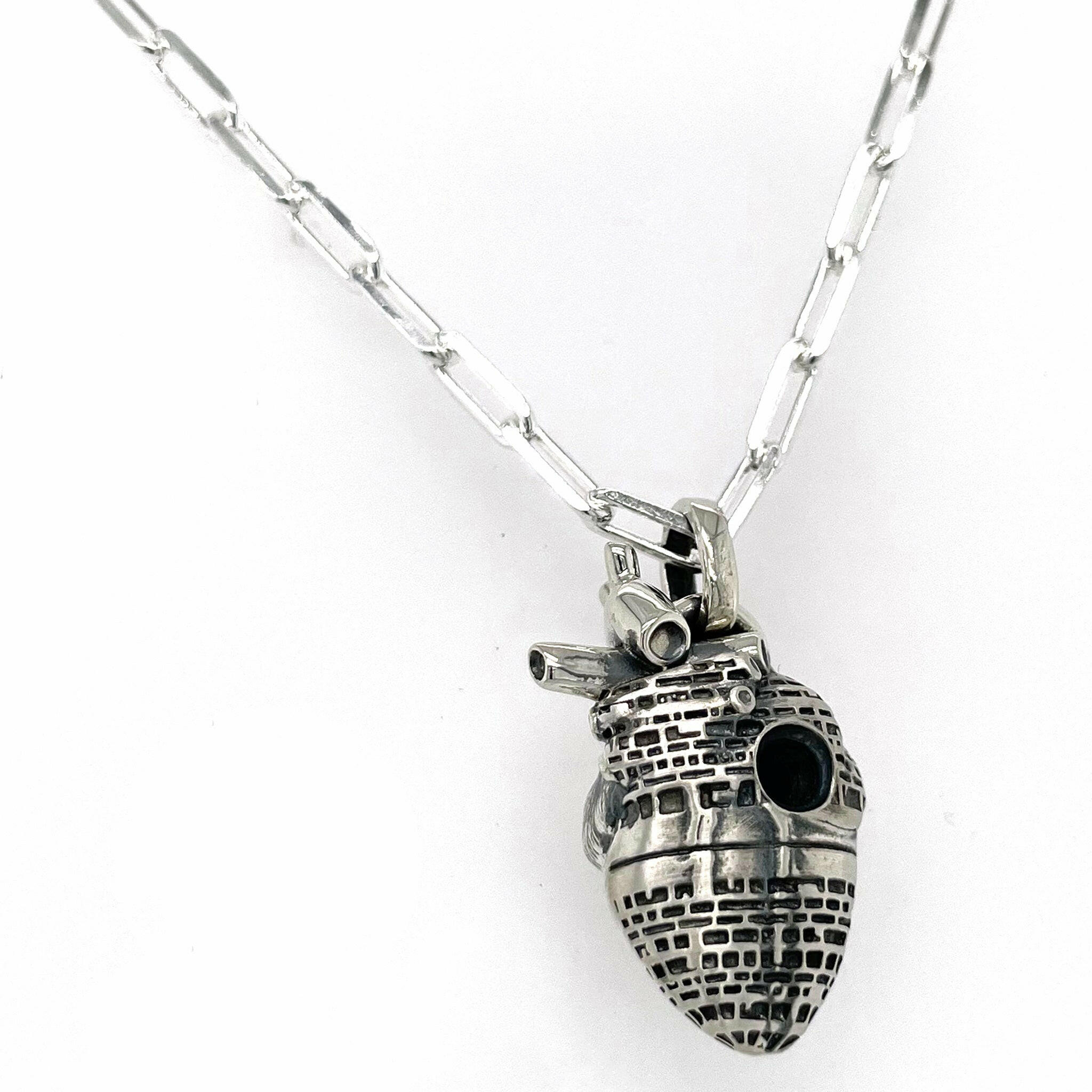 back view of fatal flaw pendant made of sterling silver , pendant resembles an atomical heart with hole in the center surrounded by an star wars like architectural design